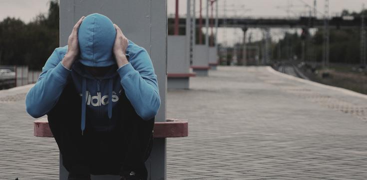 person at railway station in hoodie with head down